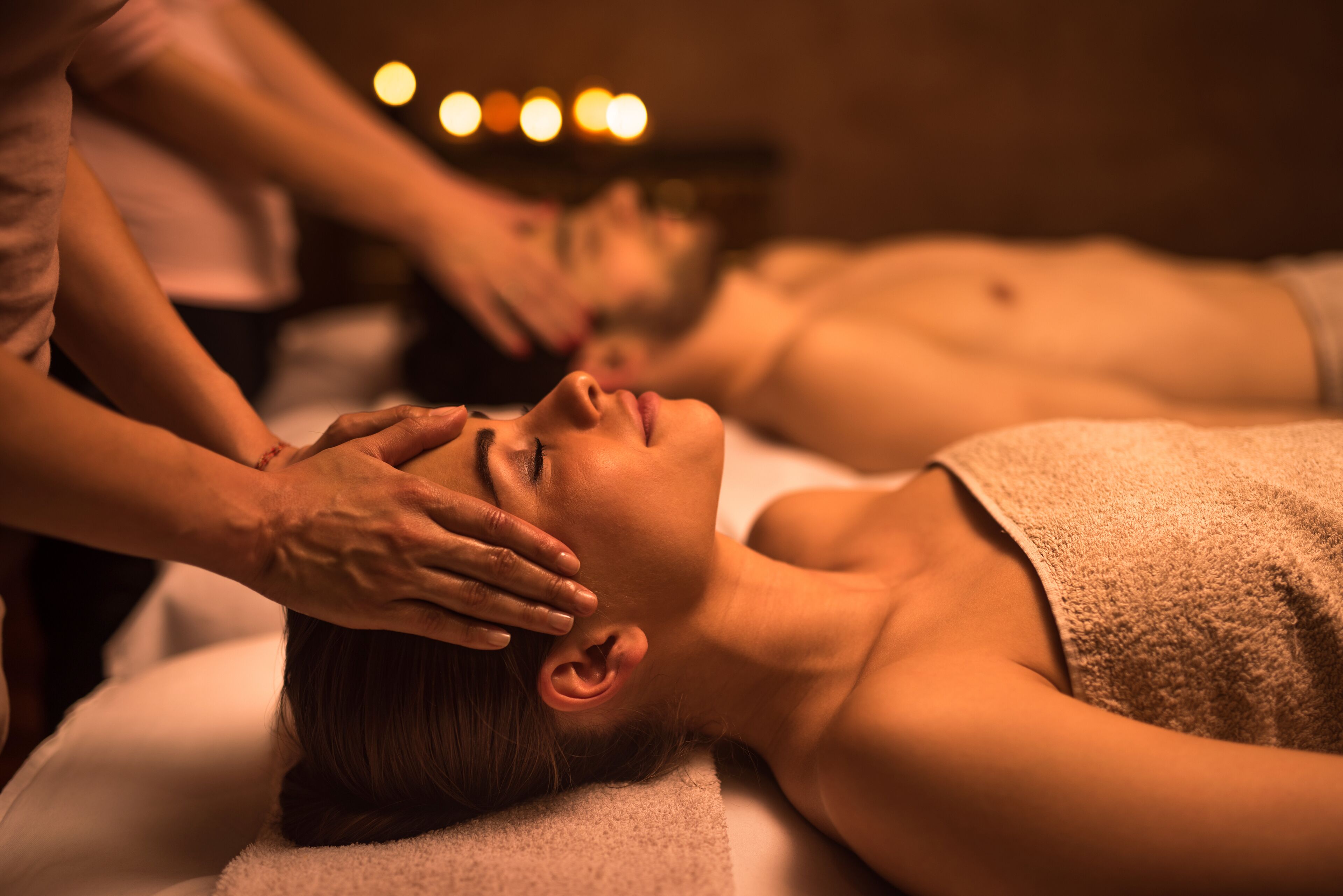 A person receiving a head massage in a dimly lit room with a massage table and a towel.