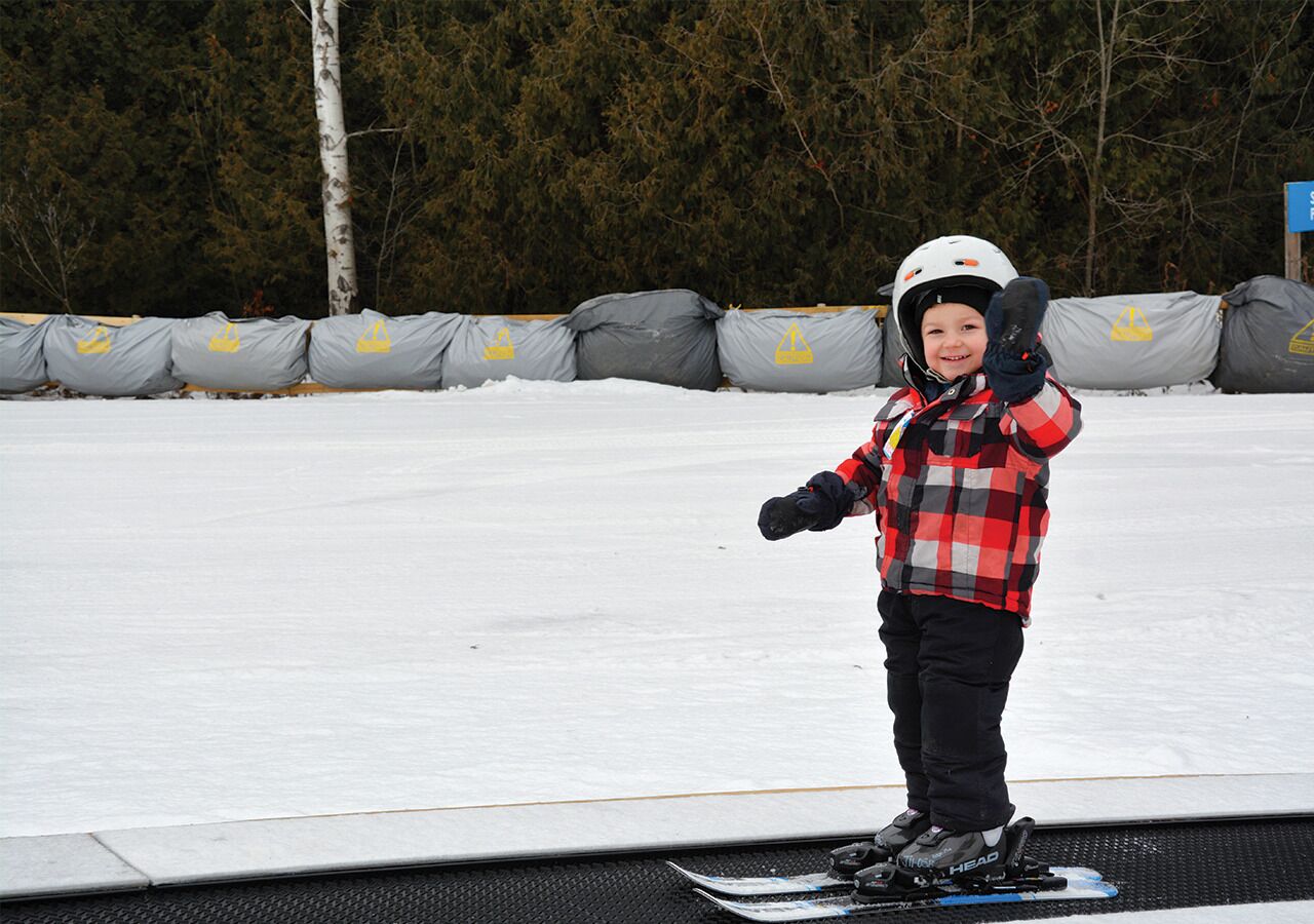 A person standing on a snowboard on a flat surface with a snowy background and trees.
