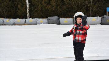 En person som står på ett snowboard på en plan yta med ett snötäckt landskap och träd i bakgrunden.