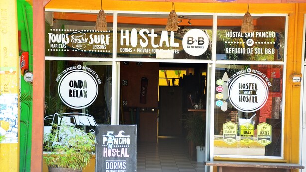 A hostel with a sign advertising tours, surf lessons, and a B&B.