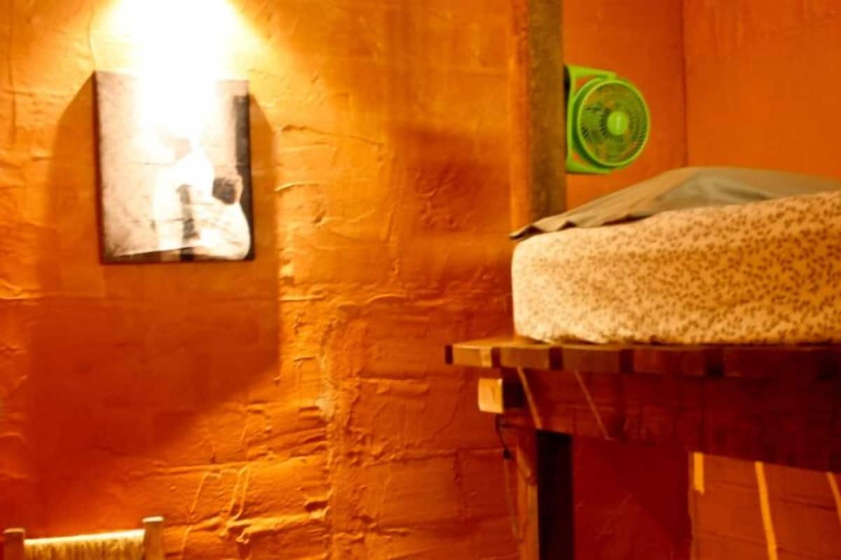 Une pièce avec un lit, une lampe fixée au mur et un ventilateur vert.