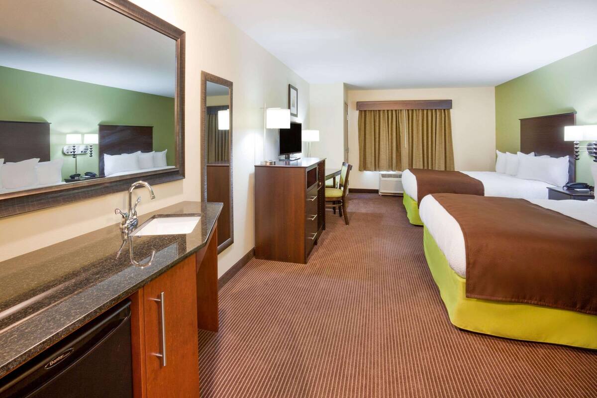 Ein Hotelzimmer mit einem großen Bett, einem Schreibtisch mit Stuhl, einem Spiegel, einem Waschbecken und einem Fenster mit Vorhängen.