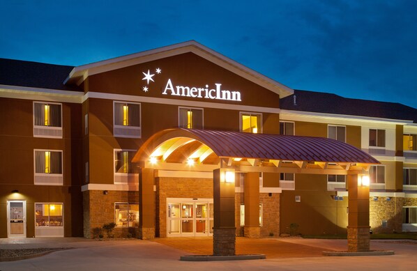Un hotel de varios pisos con un llamativo letrero de American Inn, una entrada cubierta y fachada de ladrillo.