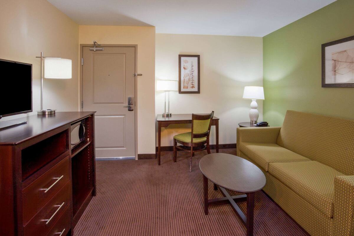 Ein Hotelzimmer mit Fernseher, einer Couch, einem Sessel, einem kleinen Tisch und einer Tür.