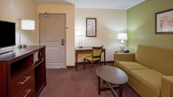 A hotel room with a television, a sofa, a chair, a small table, and a door.