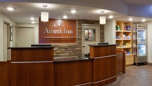 A reception desk with a wooden finish and a sign that reads "American Inn." There is a refrigerator stocked with beverages and snacks, and a small shelf with various items.
