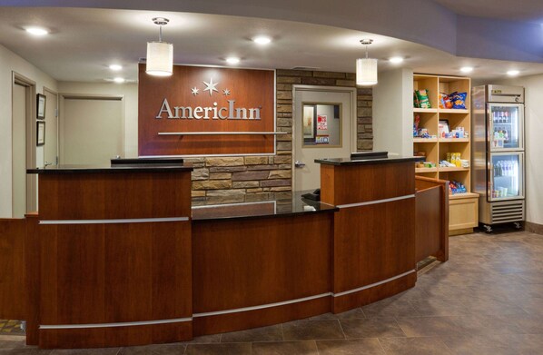 A reception desk with a wooden finish and a sign that reads "American Inn." There is a refrigerator stocked with beverages and snacks, and a small shelf with various items.