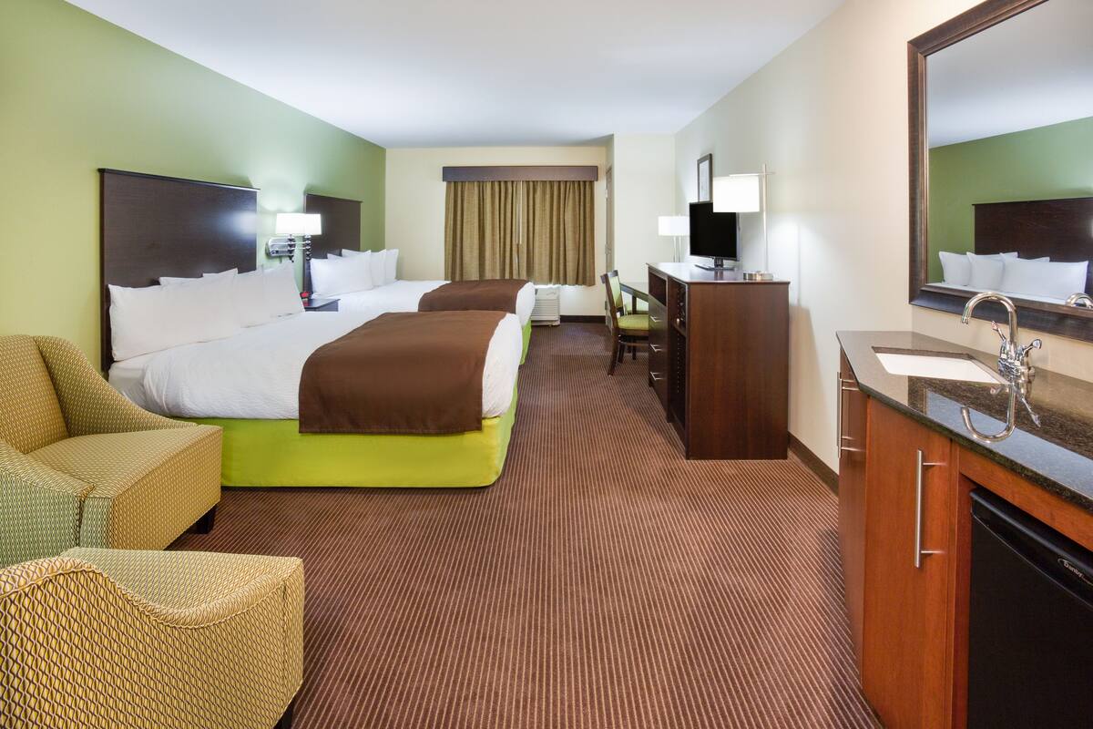 Ein Hotelzimmer mit einem großen Bett, einem Schreibtisch, einem Sessel, einer Couch und einem Badezimmer mit Waschbecken und Spiegel.
