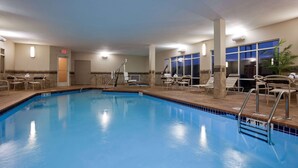 An indoor swimming pool with clear blue water, surrounded by lounge chairs and a tiled deck.