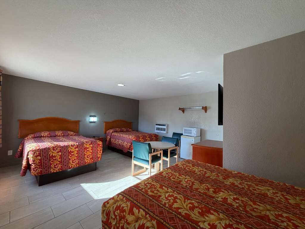 A hotel room with two beds, a desk, a chair, a microwave, and a flat-screen TV.
