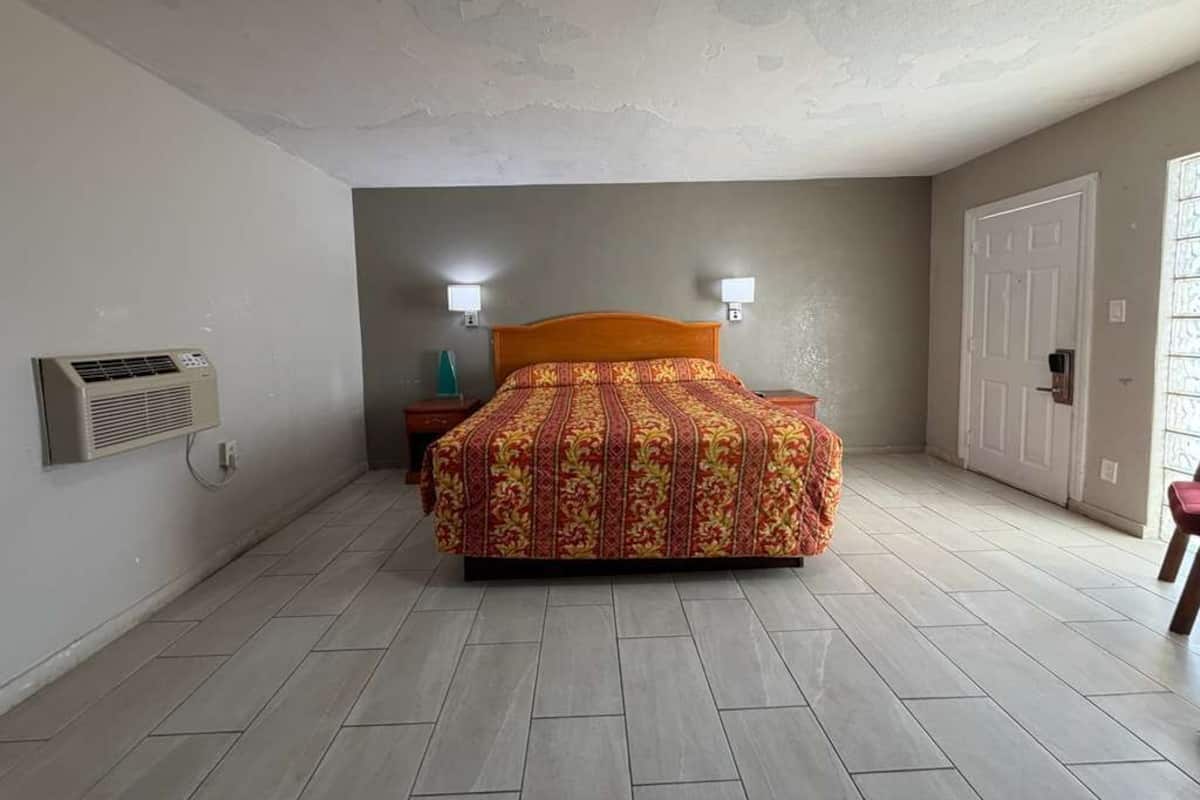 A bedroom with a bed, two bedside lamps, a door, and an air conditioning unit.