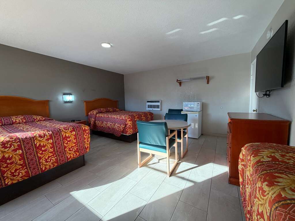 A hotel room with two beds, a desk, a chair, a TV, and an air conditioning unit.