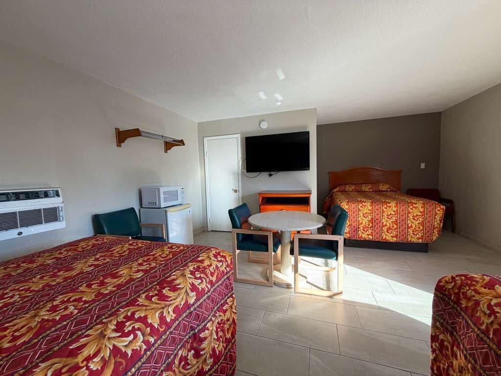 Habitación de hotel con dos camas, televisión, microondas, una mesita con sillas y una ventana.