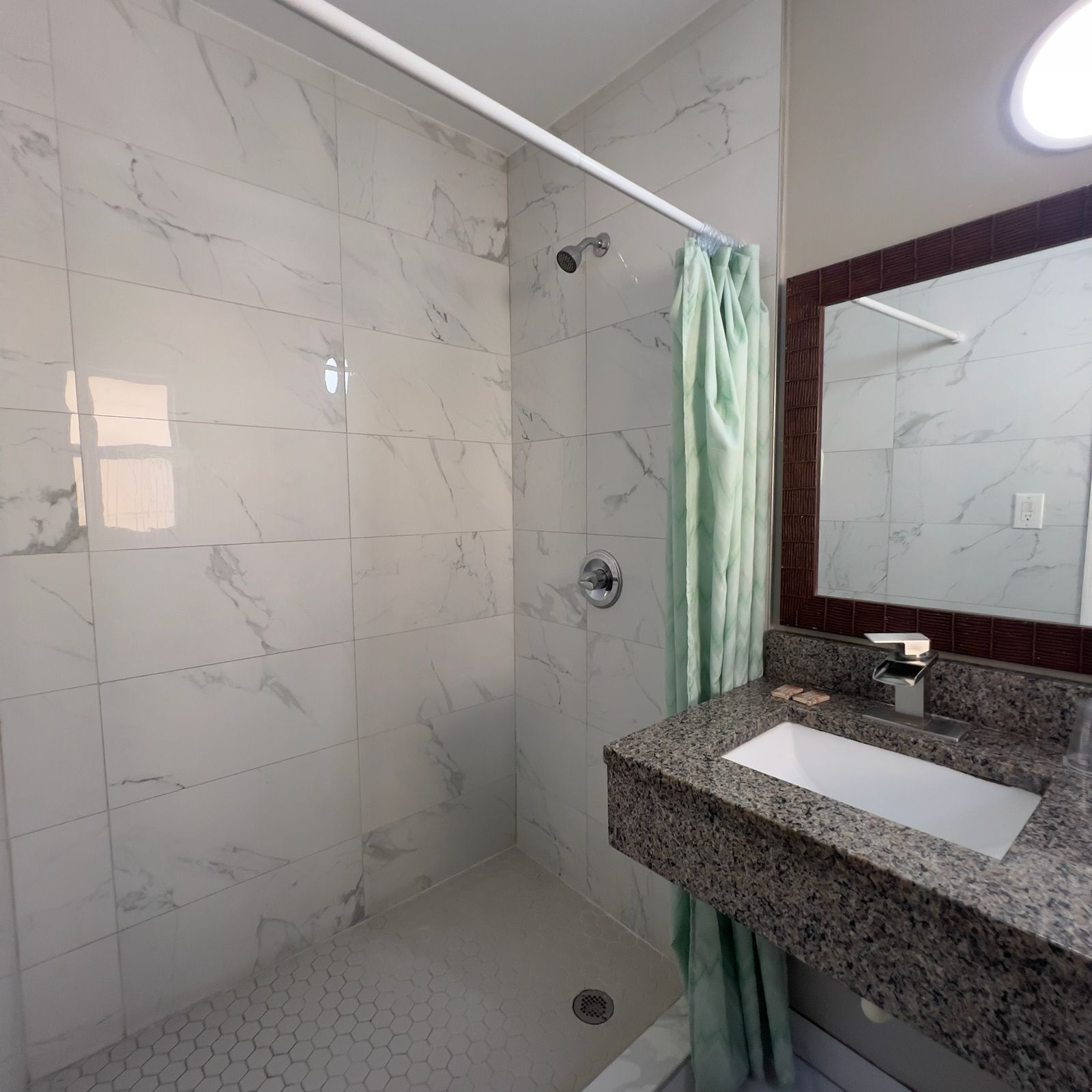 Une salle de bain avec une douche, un lavabo doté d’un plan de travail en granit et un miroir.