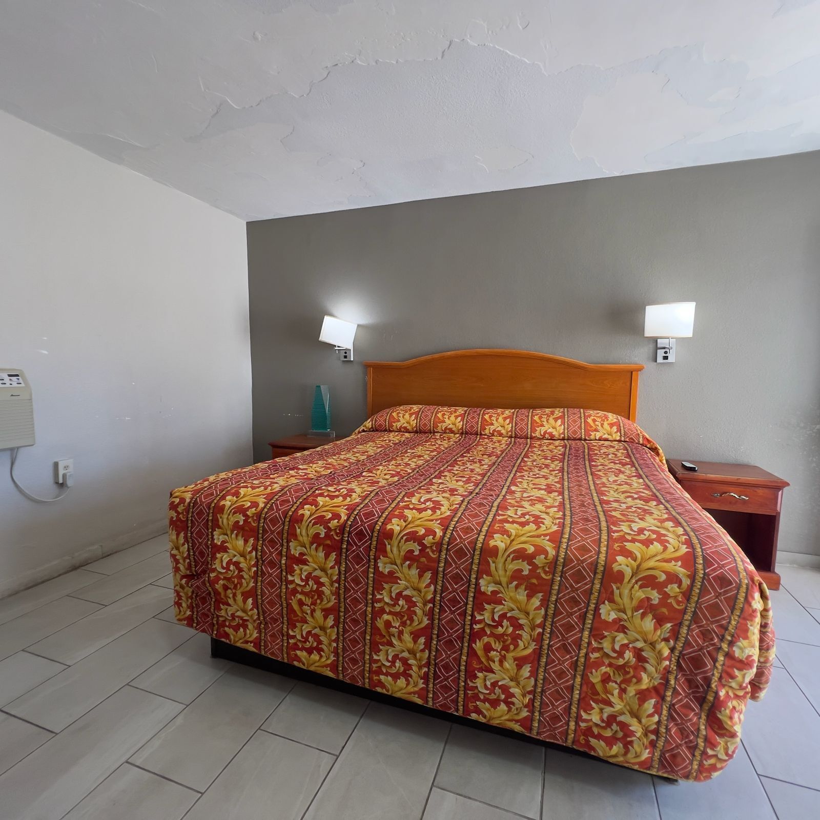 A bedroom with a bed, two bedside tables, a nightstand, a wall socket, and a light switch.