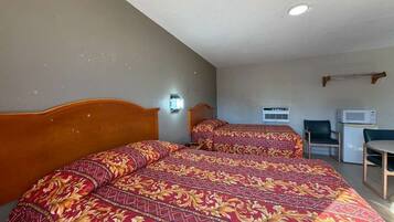 A hotel room with two beds, a desk, a chair, a microwave, and a wall-mounted air conditioning unit.