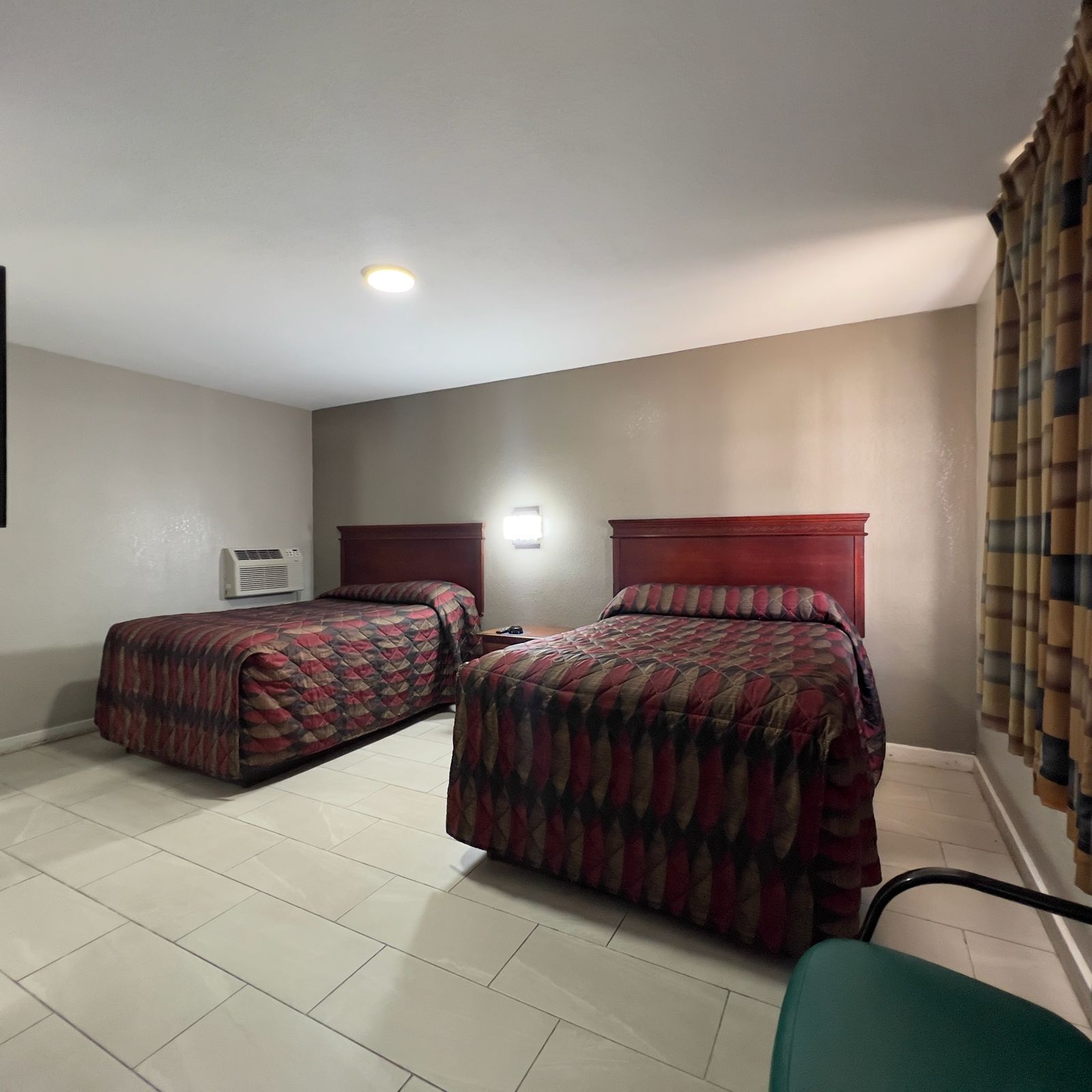 A room with two beds, a ceiling light, a wall-mounted air conditioner, and a green chair.