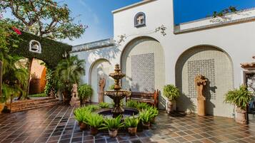 A courtyard with a fountain, potted plants, and a tiled floor.