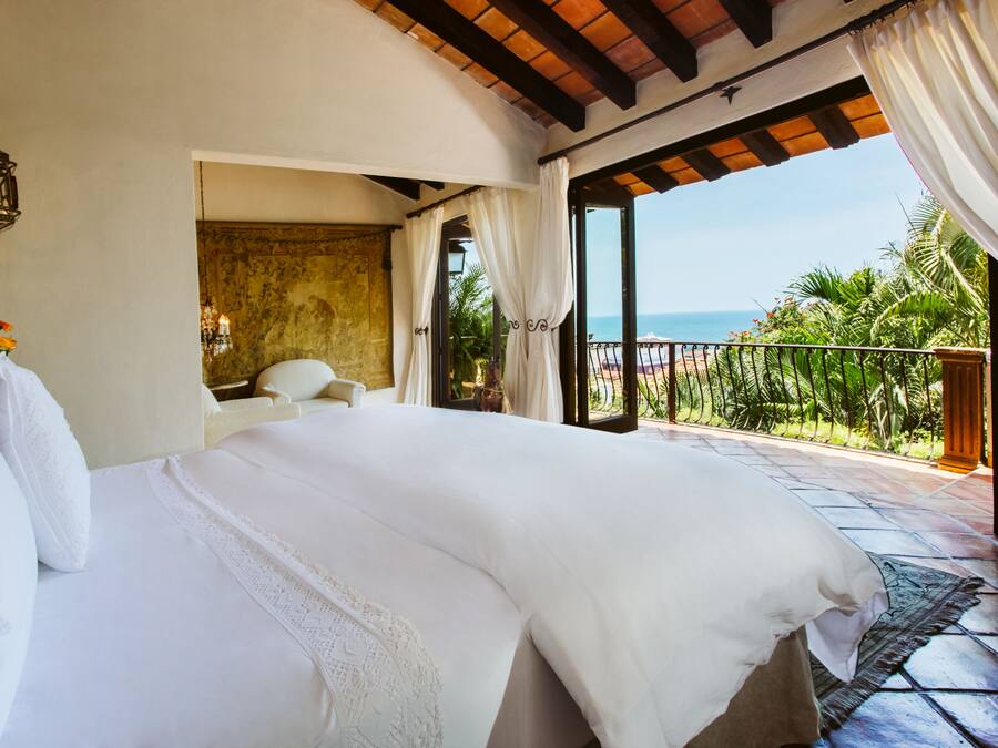 A bedroom with a large bed, a view of the ocean, and a balcony with a railing.