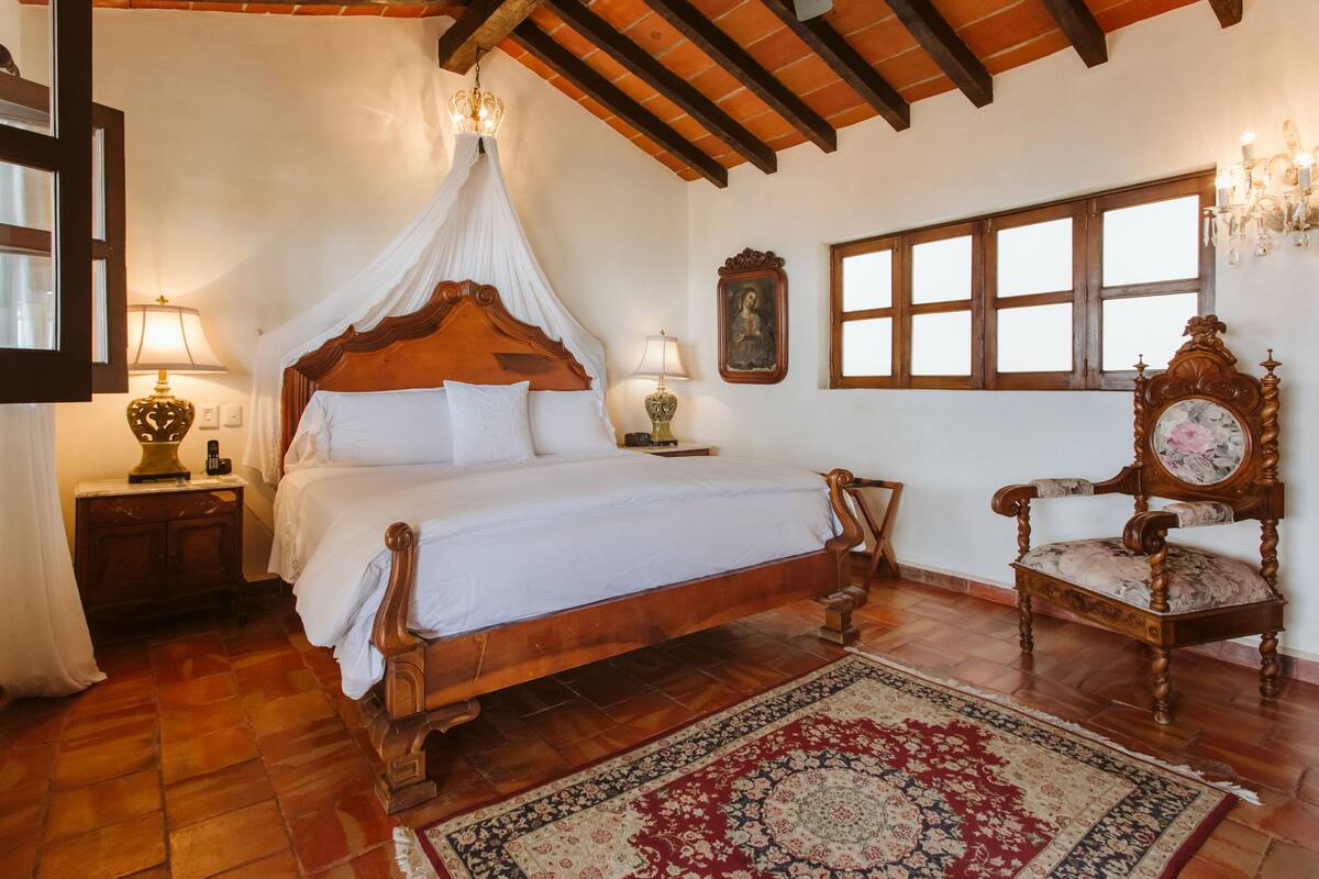 Een traditionele slaapkamer met een houten hemelbed, een groot raam en een klassieke stoel.
