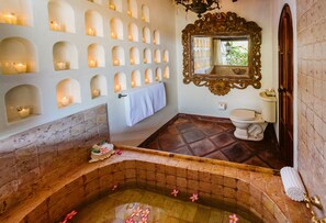 A bathroom with a bathtub, a toilet, and a wall of sconces.