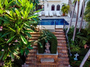 A pool area with a statue, white chairs, and lush greenery.