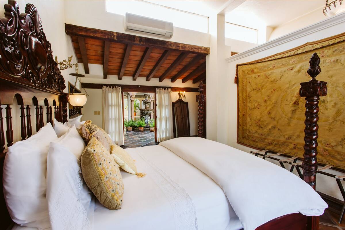 Een slaapkamer met een groot bed, een houten hoofdbord en uitzicht op een binnentuin met planten.