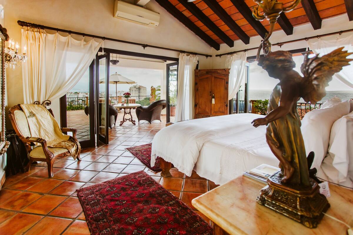 Een hotelkamer met een bed, een stoel, een tafel en een beeld. Er is een balkon met uitzicht op de oceaan.