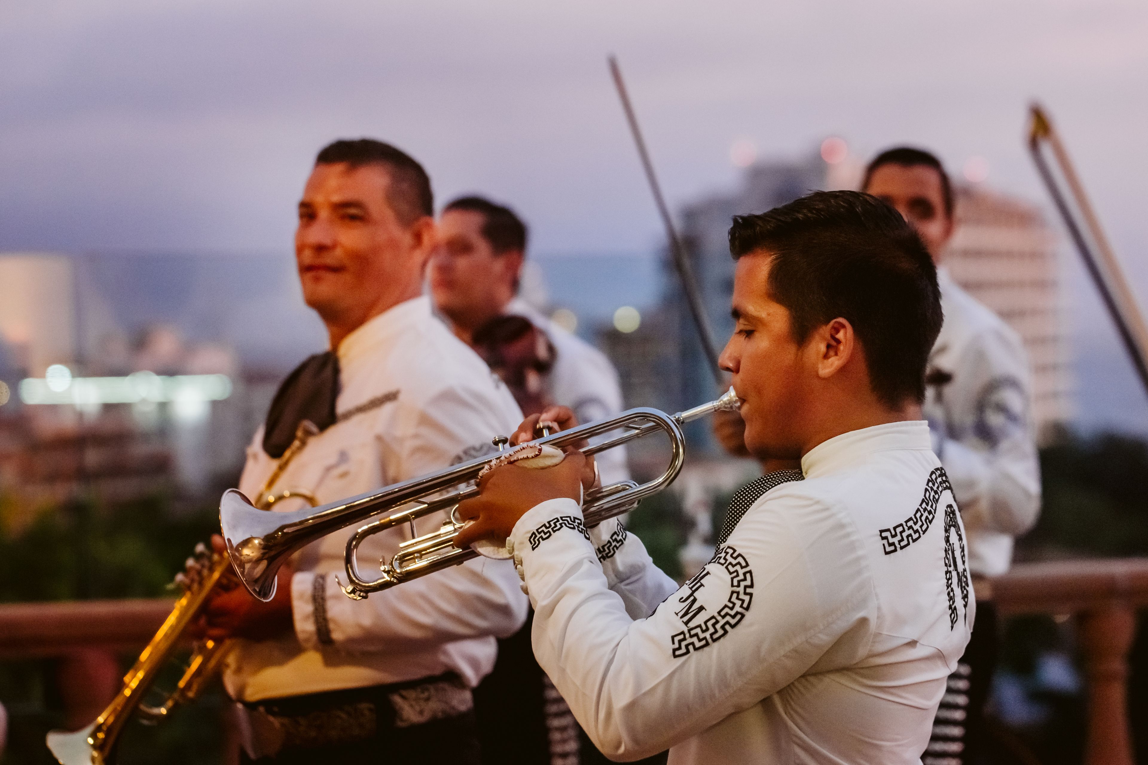 Un grupo de músicos con vestimenta tradicional tocando instrumentos de viento metal.