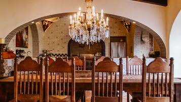 Un comedor con una gran mesa de madera y sillas, una araña y un rebozado de azulejos.