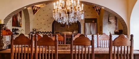 A dining area with a large wooden table and chairs, a chandelier, and a tiled backsplash.