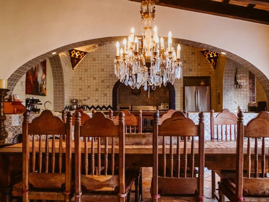 Un comedor con una gran mesa de madera y sillas, una araña y un rebozado de azulejos.