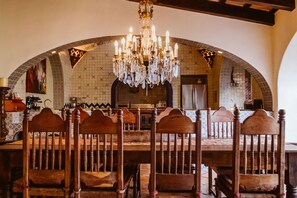 A dining area with a large wooden table and chairs, a chandelier, and a tiled backsplash.