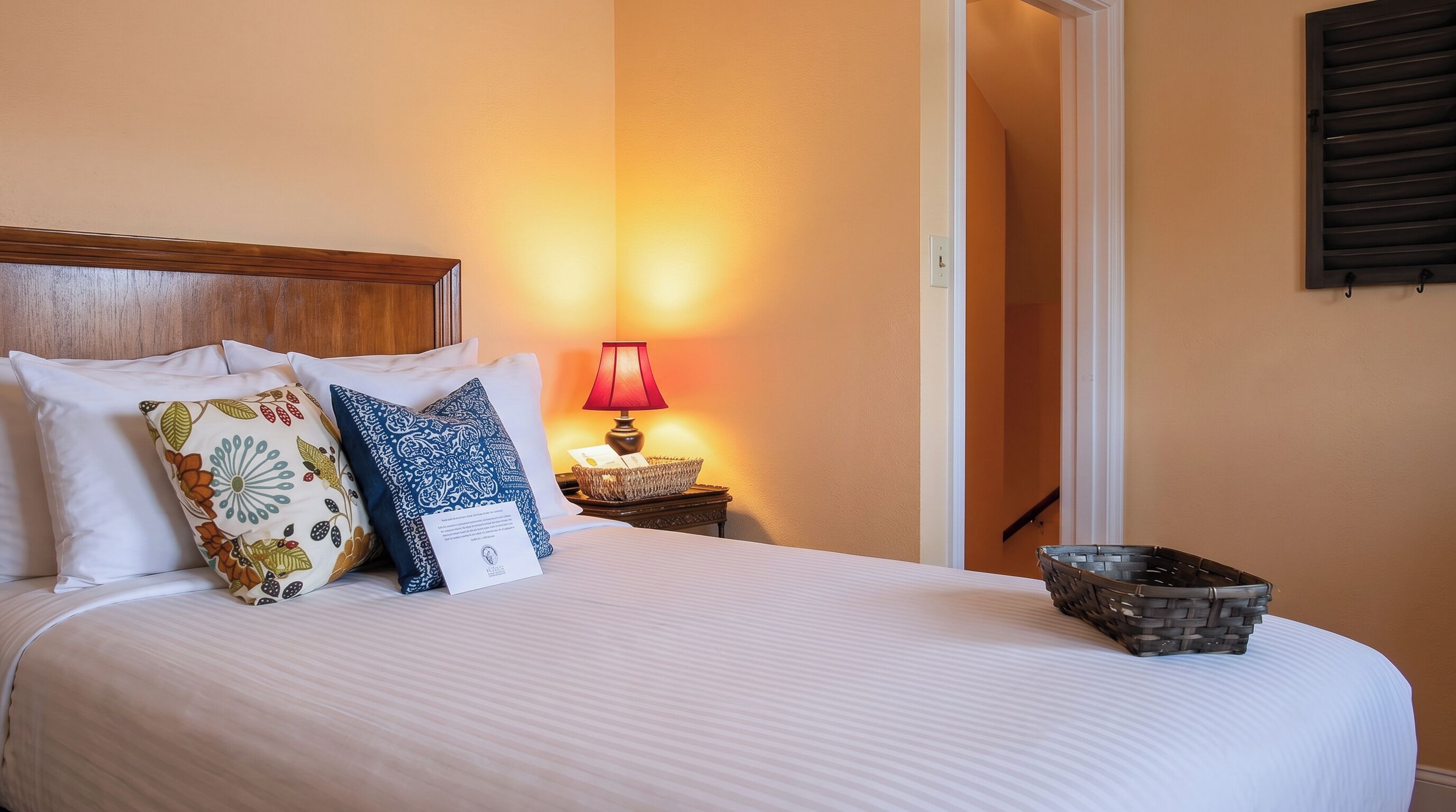 A neatly made bed with pillows, a bedside lamp, and a small basket on the nightstand.