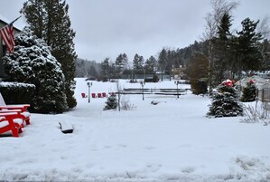 Un espacio exterior cubierto de nieve con un banco rojo, un pequeño árbol de Navidad y una valla.
