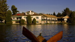 A lakeside hotel with a large building, a dock, and a row of boats.