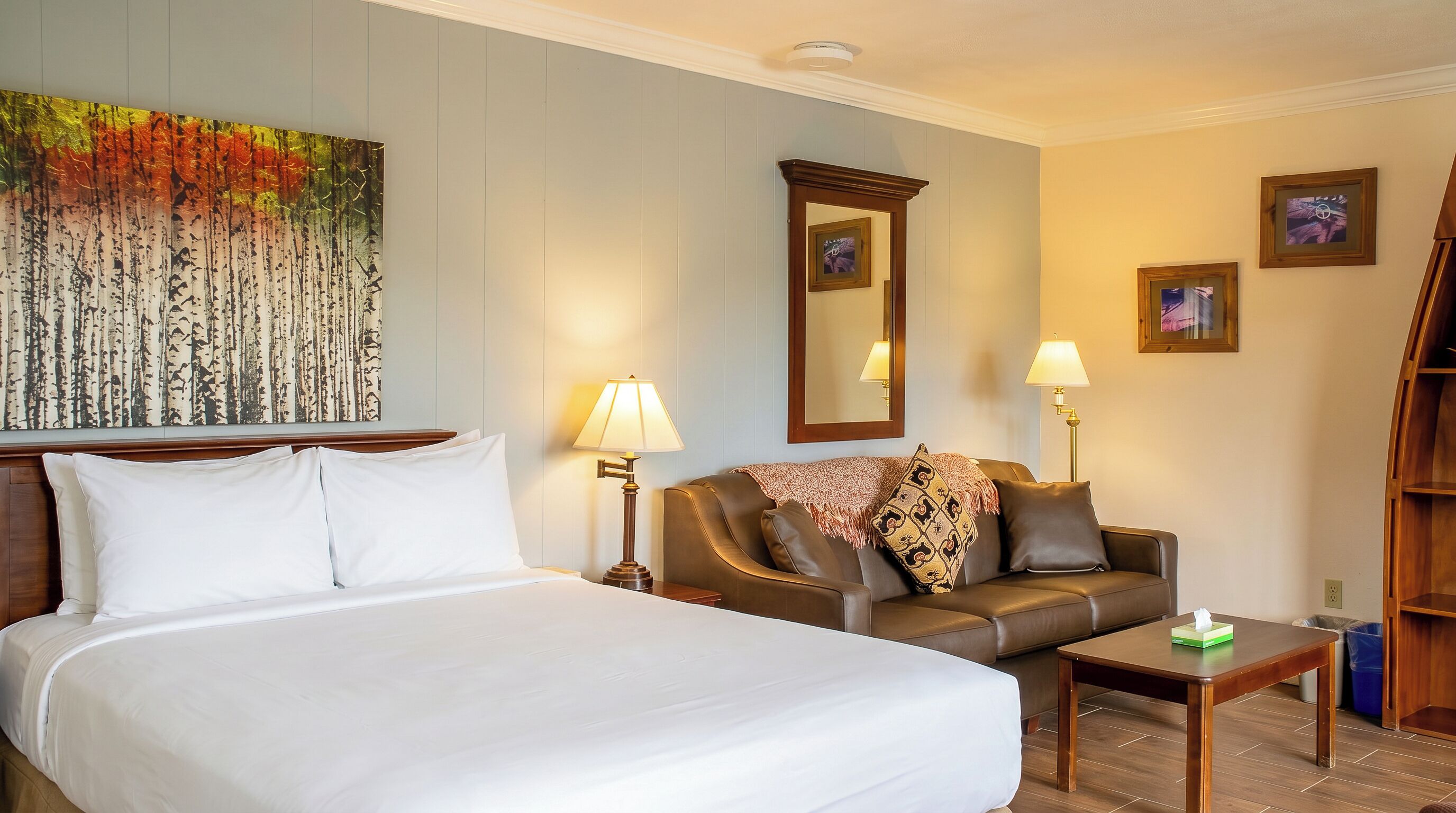 A hotel room with a large bed, a sofa, two lamps, a mirror, and a painting on the wall.