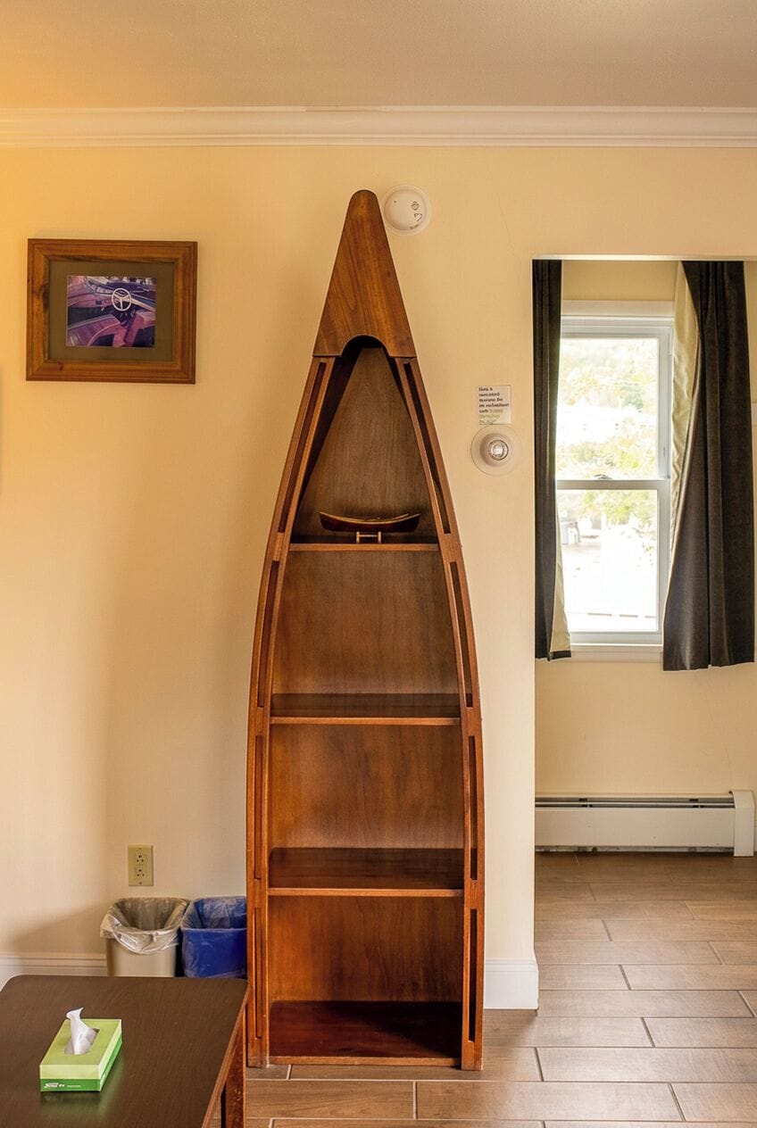 Une pièce avec une étagère en bois en forme de bateau, un tableau encadré au mur, une fenêtre avec des rideaux et une poubelle.