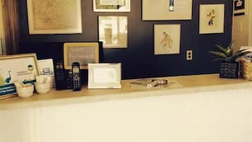 Un mostrador de recepción con obras de arte enmarcadas, un letrero que dice "ENTER AS STRANGER, LEAVE AS FRIENDS." y una planta en maceta.