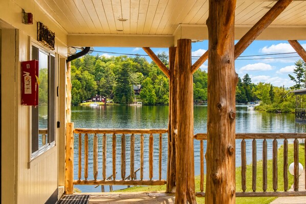 A wooden deck with a railing overlooking a lake, surrounded by trees and a small dock. - Gauthier's Saranac Lake Inn (Saranac Lake)