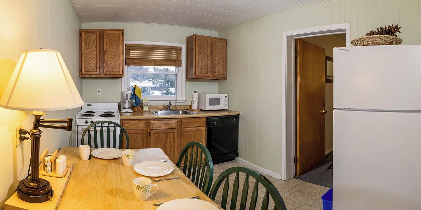 A compact kitchen with wooden cabinets, a microwave, a stove, and a dining table set for four.