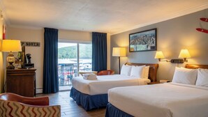 A hotel room with two beds, a desk with a lamp, a chair, and a view of a dock with boats.