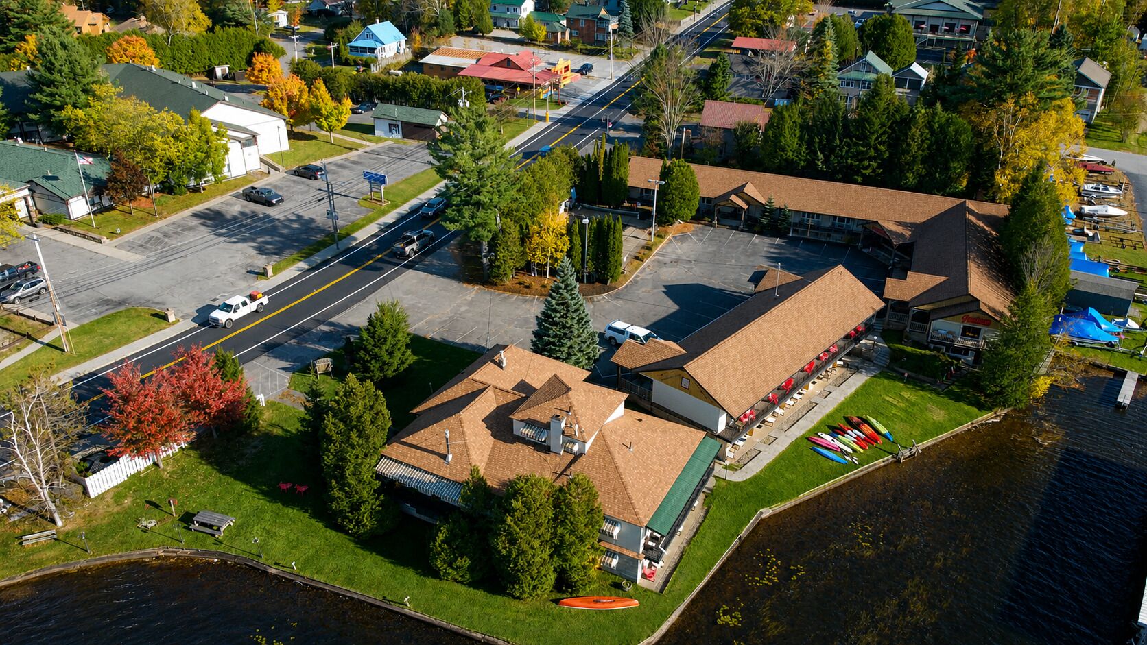An aerial view of a lakeside property with a large building, parking lot, and boats docked by the water.