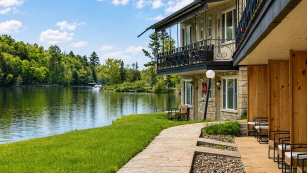 A lakeside hotel with a stone facade, outdoor seating, and a balcony overlooking the water.