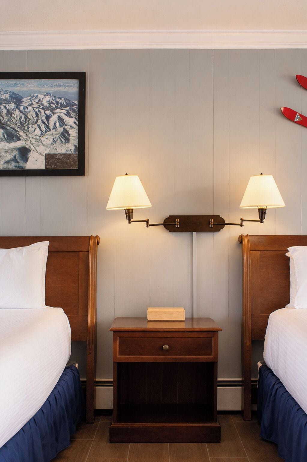 A hotel room with two beds, a nightstand with a lamp, a framed picture on the wall, and a red object on the ceiling.