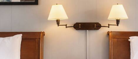 A hotel room with two beds, a nightstand with a lamp, a framed picture on the wall, and a red object on the ceiling.