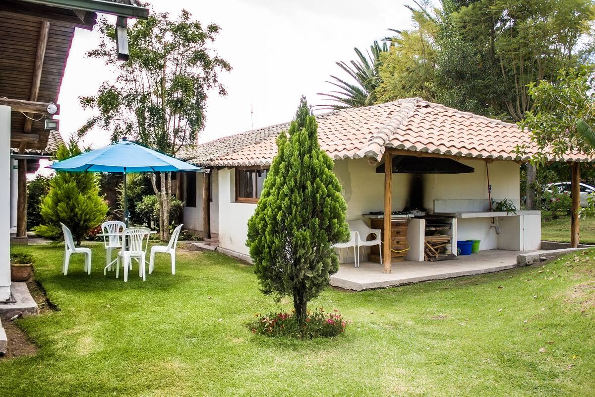 Una casa con techo de tejas, un patio con un paraguas azul y un pequeño árbol en el jardín.