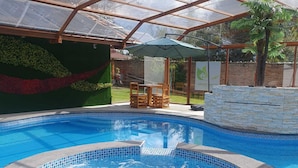Una piscina con hidromasaje, rodeada por una zona acristalada con un muro de piedra y un muro verde con plantas.