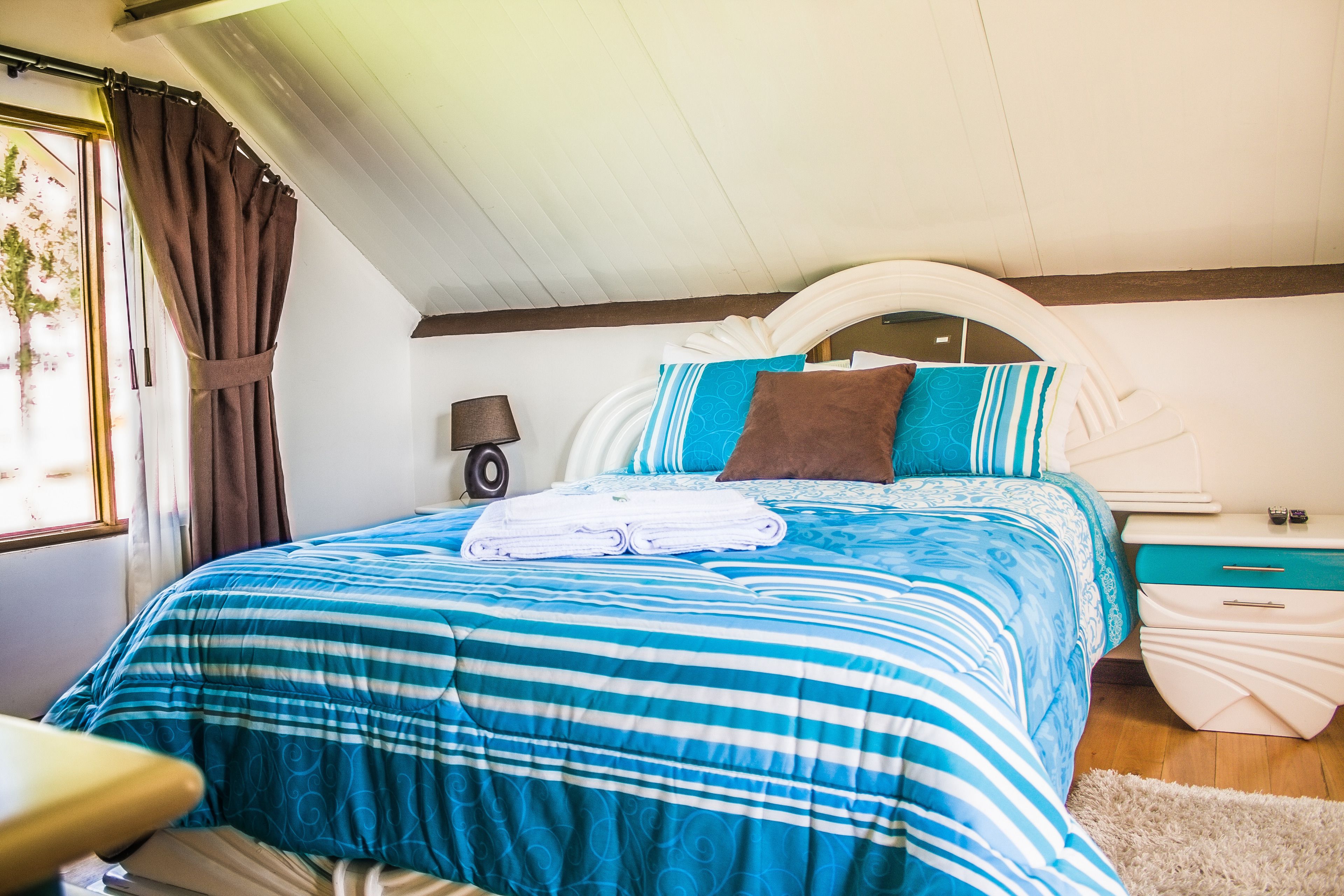 A bedroom with a bed, nightstands, a lamp, and a window with curtains.