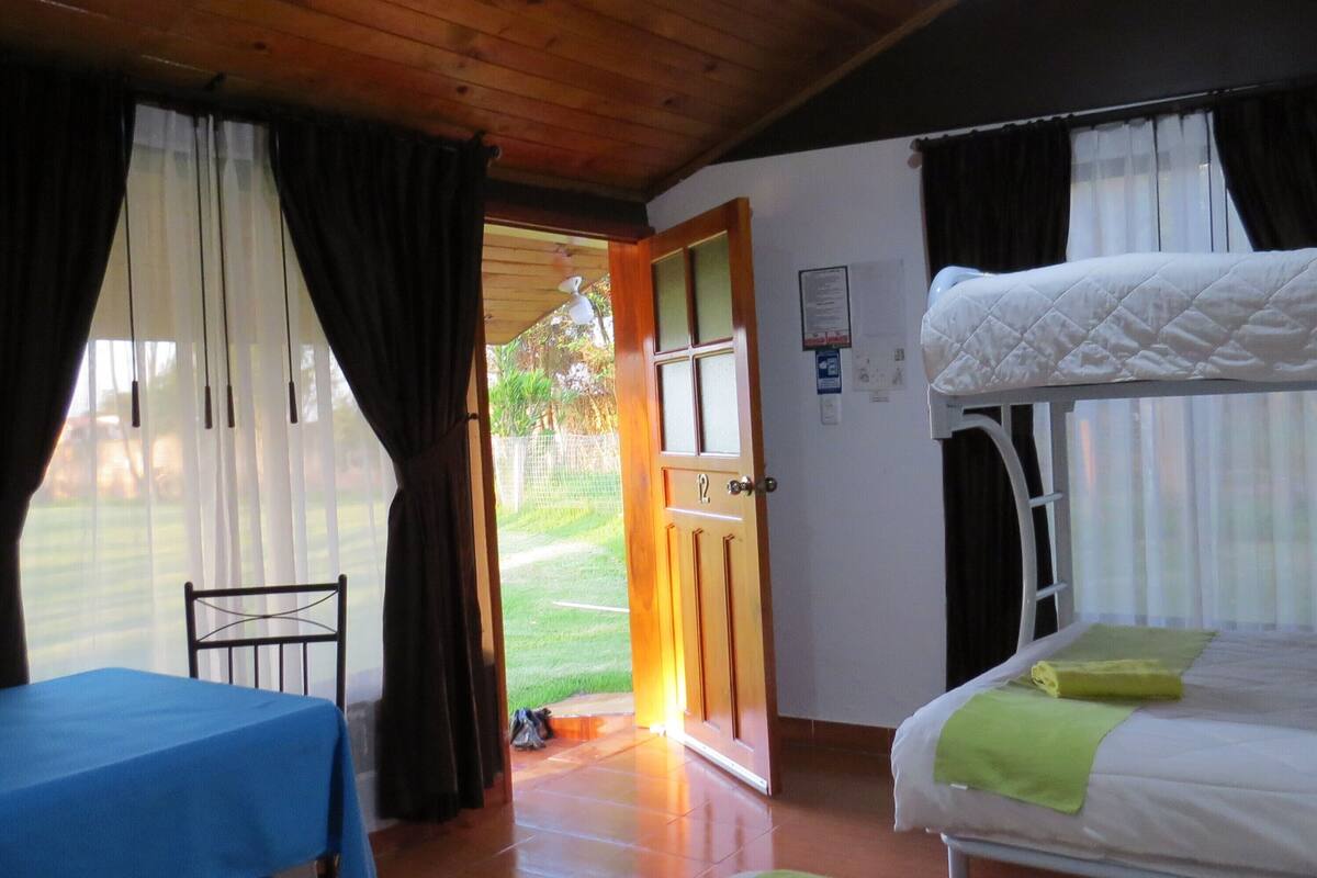 Habitación con literas, una mesa y una silla. Hay una puerta que da al exterior.